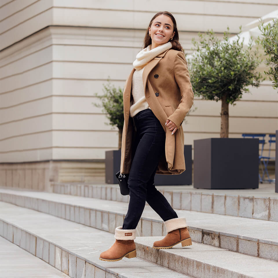 Žena v elegantnom kabáte obúva vysoké izolované topánky NOEL na mestských schodoch.