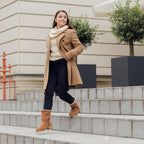 Žena v béžovom kabáte nosí vysoké izolované topánky NOEL a kráča po schodoch v meste.