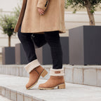 Osoba v kabáte obúva vysoké izolované topánky NOEL v hnedej farbe na mestskom chodníku.